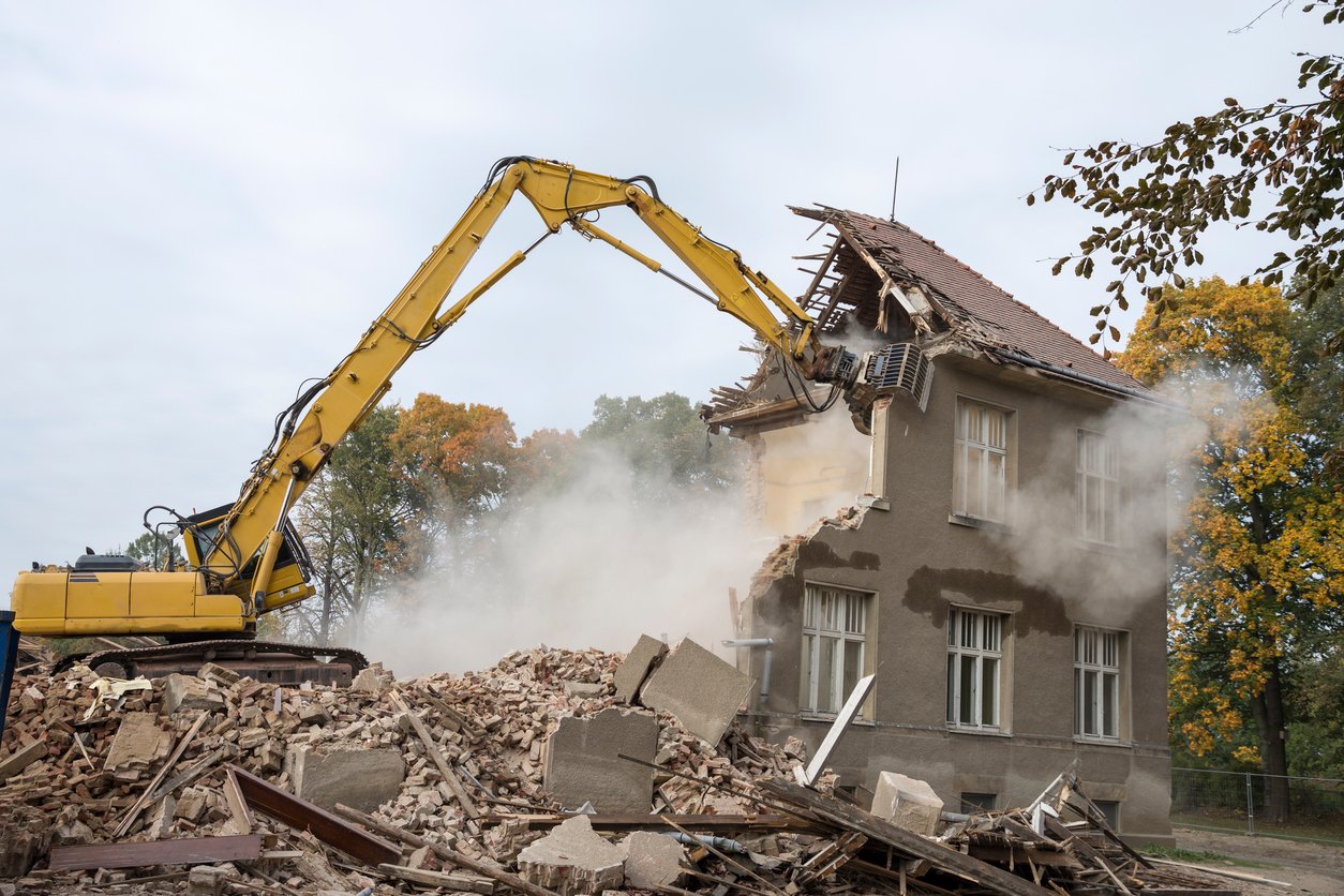 Excavator sitting on rubble demolishing a house